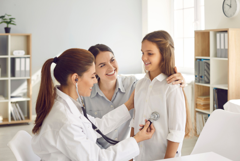 Female doctor pediatrician using stethoscope listens lungs and heart of child girl. Doctor or nurse examines teen girl who came for medical examination with her mother. Concept of pediatric medicine.